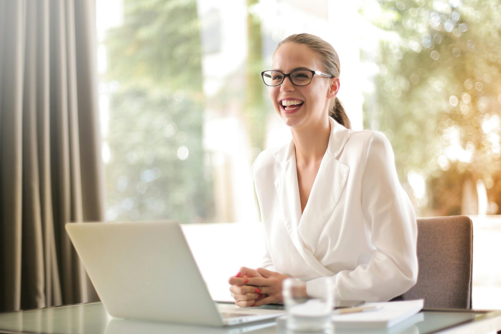 An office lady sitting in front of a laptop and seems to laugh at a discussion